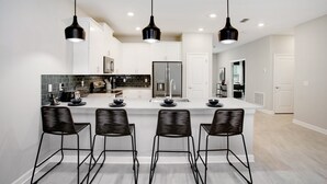 A modern kitchen with a central island, black bar stools, and pendant lighting. - 9BR Villa with Game Room & Theater (Kissimmee)