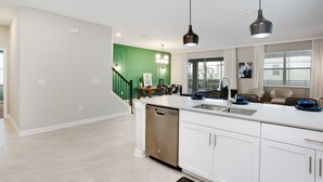 A modern kitchen with white cabinets, a dishwasher, and a large island with a sink. - 9BR Villa with Game Room & Theater (Kissimmee)