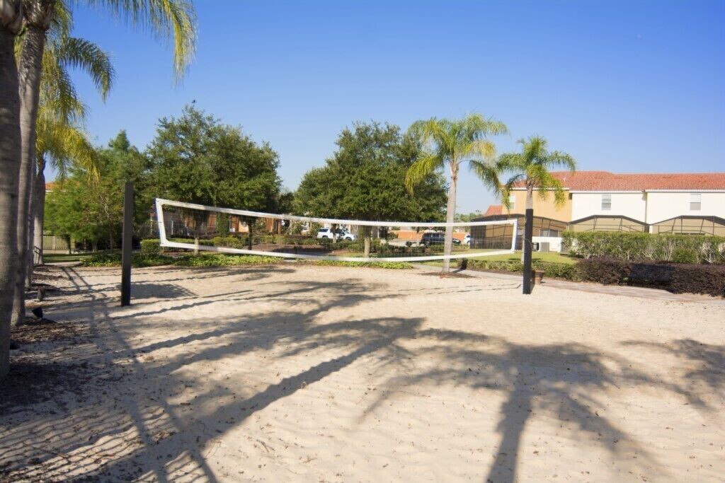 A sandy volleyball court with a net, surrounded by palm trees and buildings.