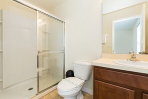 A bathroom with a glass shower enclosure, a toilet, and a sink with a mirror above it. - Bella Vida 4568 IHR 1021 (Kissimmee)