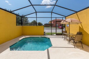 A covered outdoor swimming pool with a glass enclosure, a table and chairs, and a view of a building in the background. - Bella Vida 4568 IHR 1021 (Kissimmee)