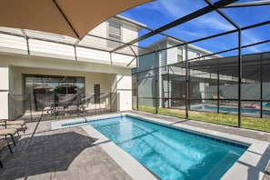 A swimming pool with a glass enclosure, patio furniture, and a covered seating area.