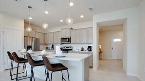 Une cuisine moderne avec des meubles blancs, des appareils en acier inoxydable et un îlot central doté de tabourets de bar.
