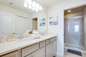 A modern bathroom with a double sink vanity, a large mirror, and a glass shower enclosure.