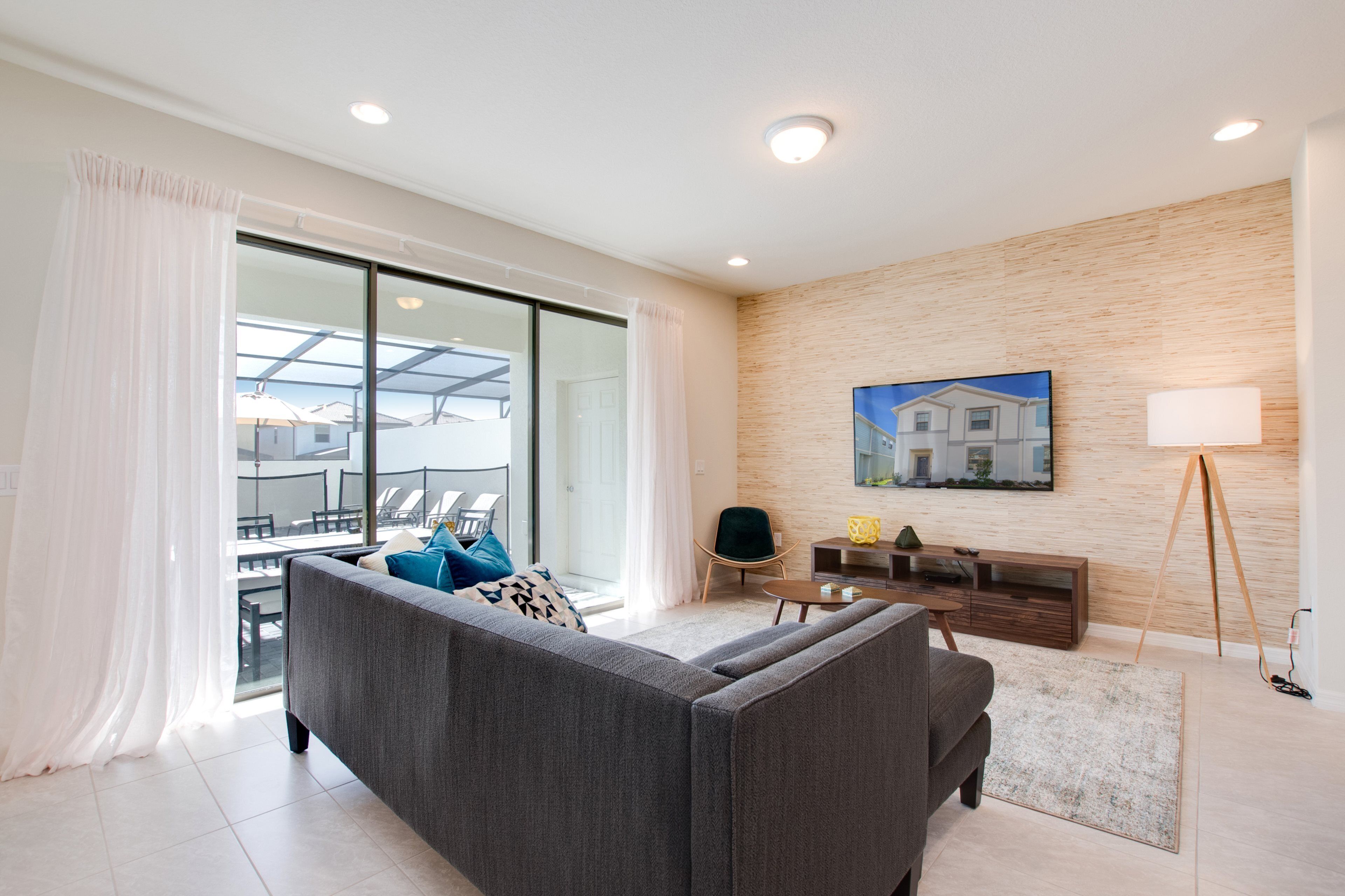 A modern living room with a grey sofa, a wooden TV stand, and a large window with curtains.
