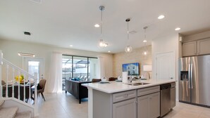 Une cuisine moderne dotée d’un îlot central, d’appareils électroménagers en acier inoxydable et de luminaires suspendus.