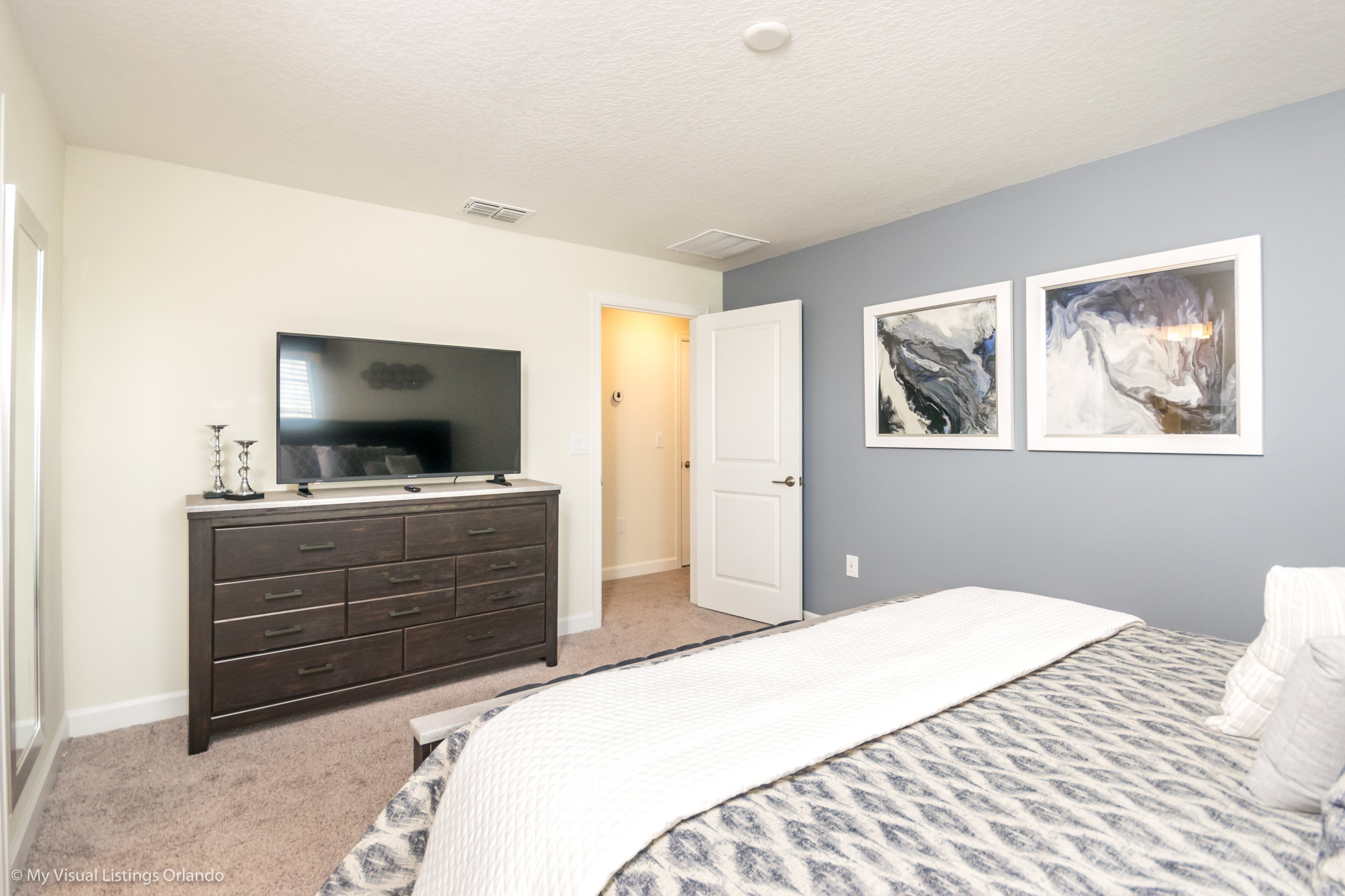 A bedroom with a bed, dresser, TV, and artwork on the wall.