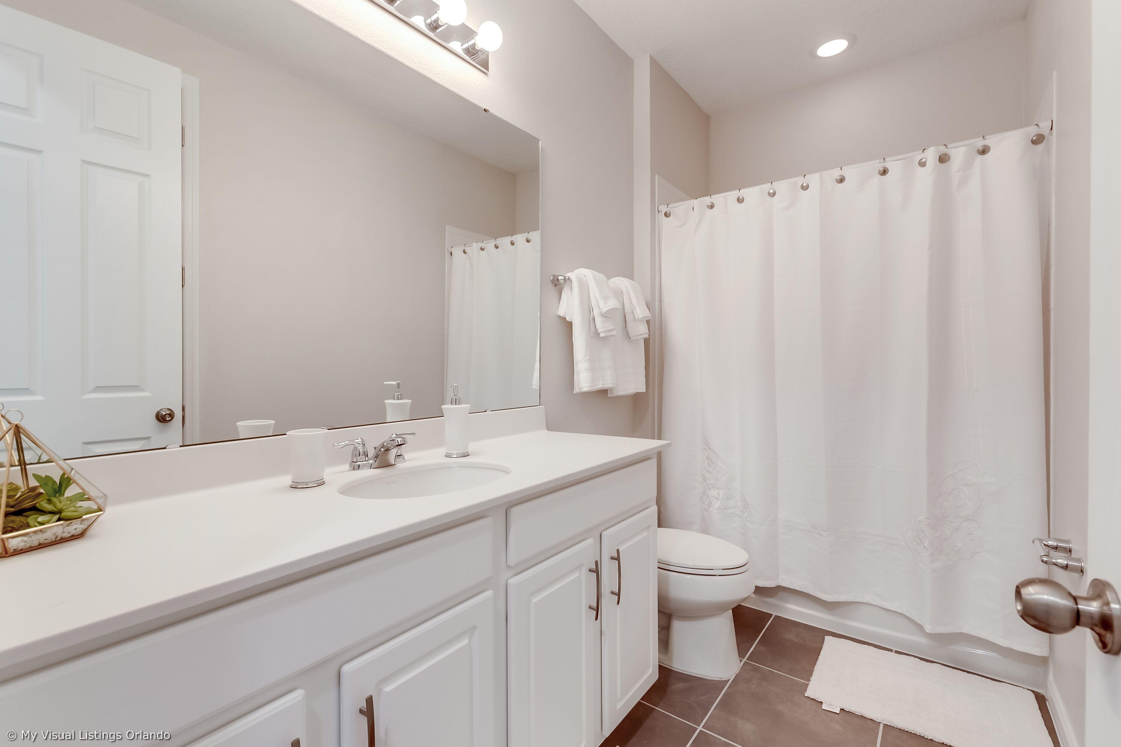 Une salle de bain avec un meuble-lavabo blanc, un évier, un miroir, des toilettes et un rideau de douche.