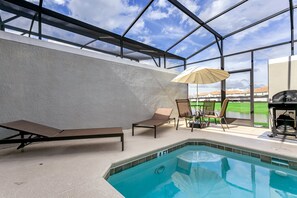 An indoor swimming pool with lounge chairs and an umbrella, surrounded by a glass enclosure with a view of a green landscape. - 4885romeo (Kissimmee)