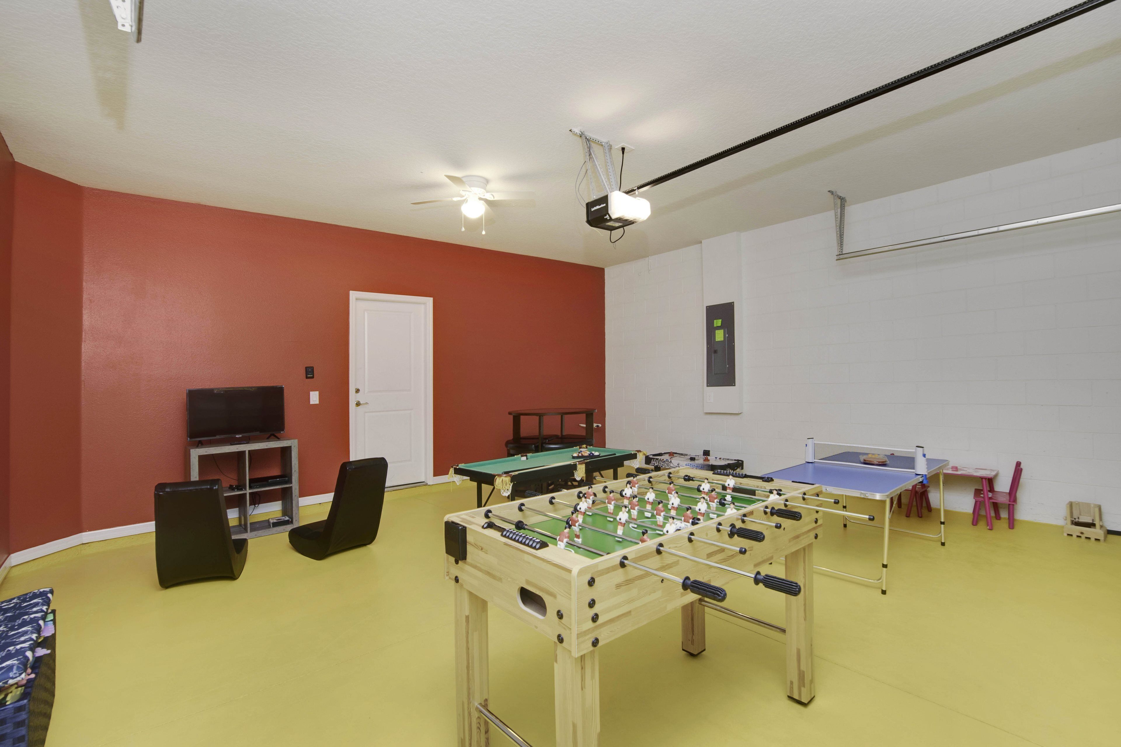 A room with a foosball table, ping pong table, and a television.