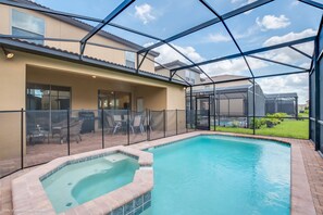 A swimming pool with a hot tub, enclosed patio with chairs, and a covered area with a grill.