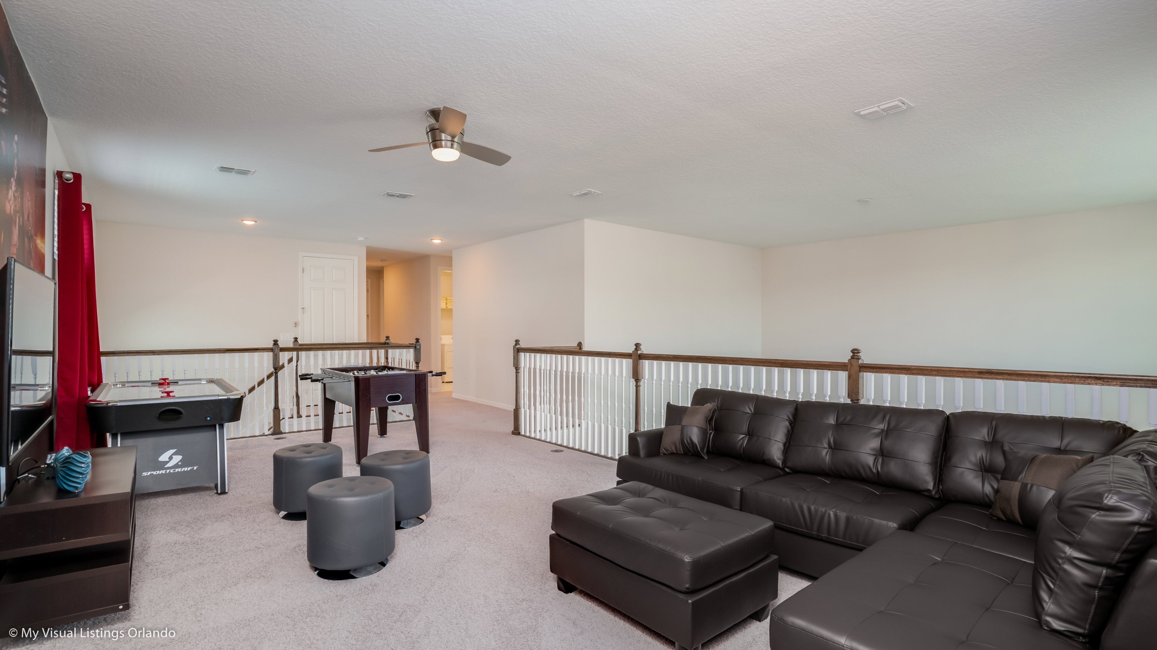 A spacious living room with a leather sofa, ottomans, a foosball table, and a ceiling fan.