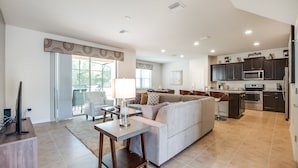 A spacious living room with a sofa, a coffee table, and a TV. There is a kitchen area with dark cabinets and a microwave. - 5bed 5Ba Villa Game Room Pool Spa (Kissimmee)