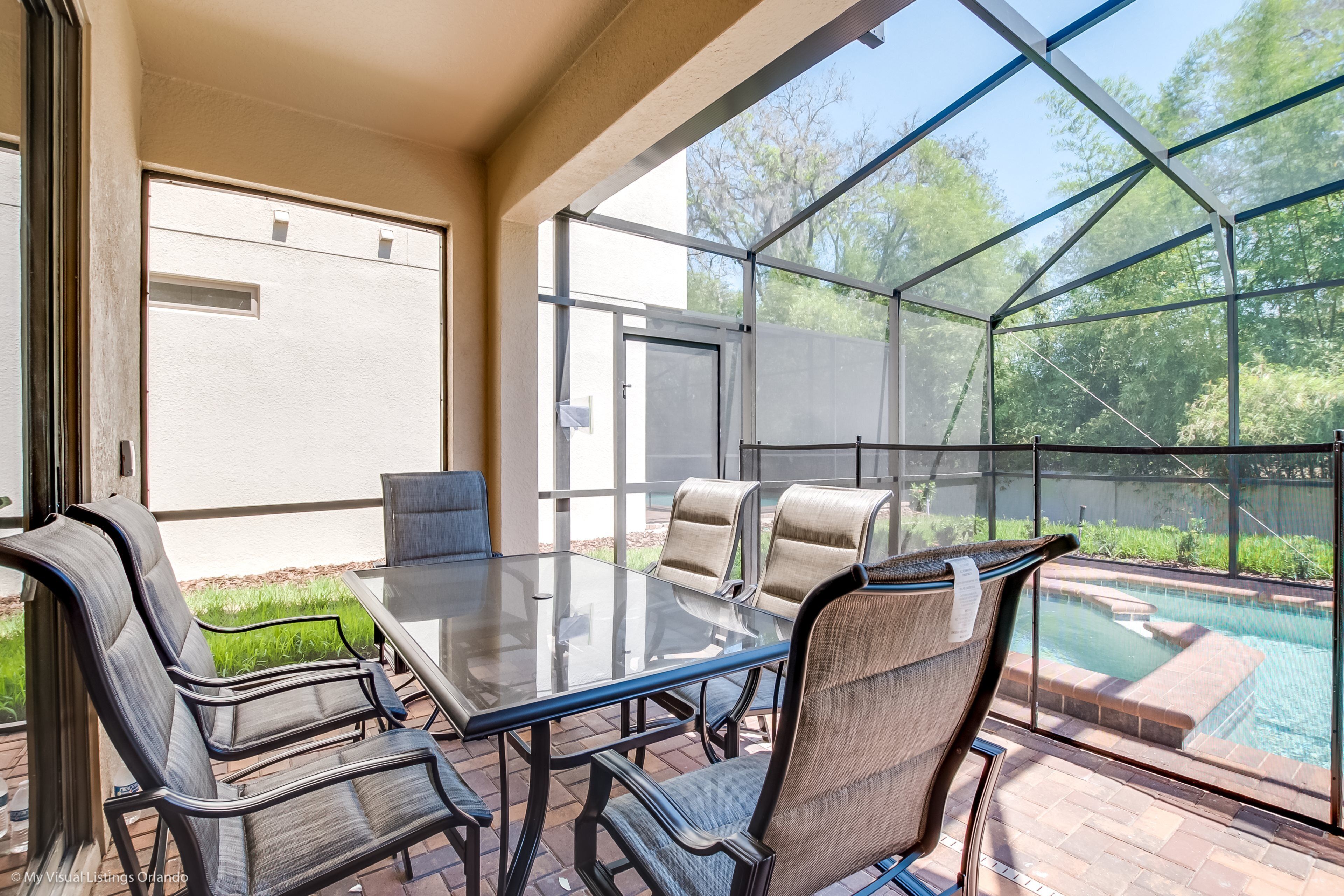 An outdoor patio with a glass table and chairs, a pool, and a covered area with a door.