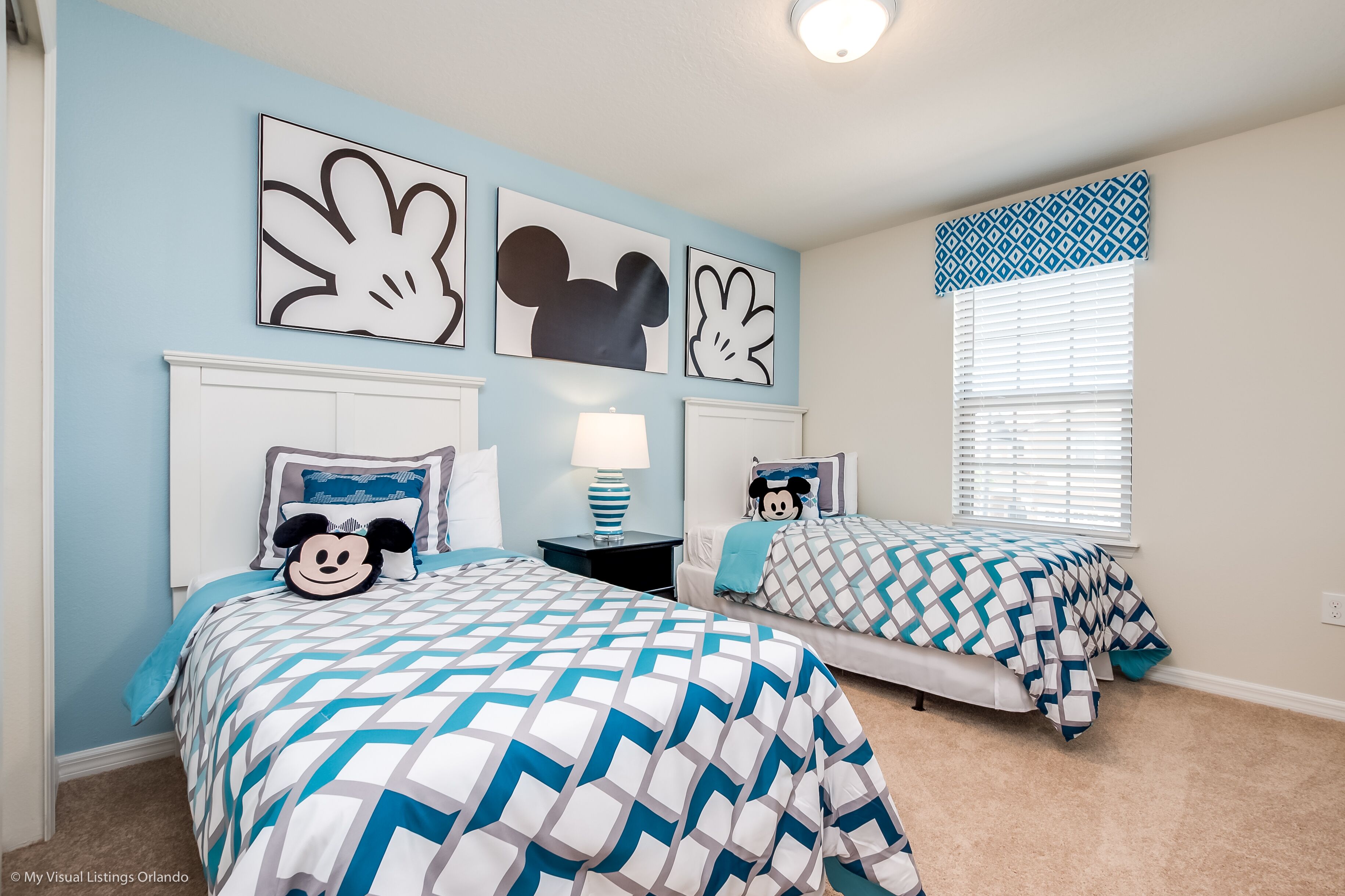 A bedroom with two beds, each with Mickey Mouse-themed bedding, a nightstand with a lamp, and wall art featuring Mickey Mouse.