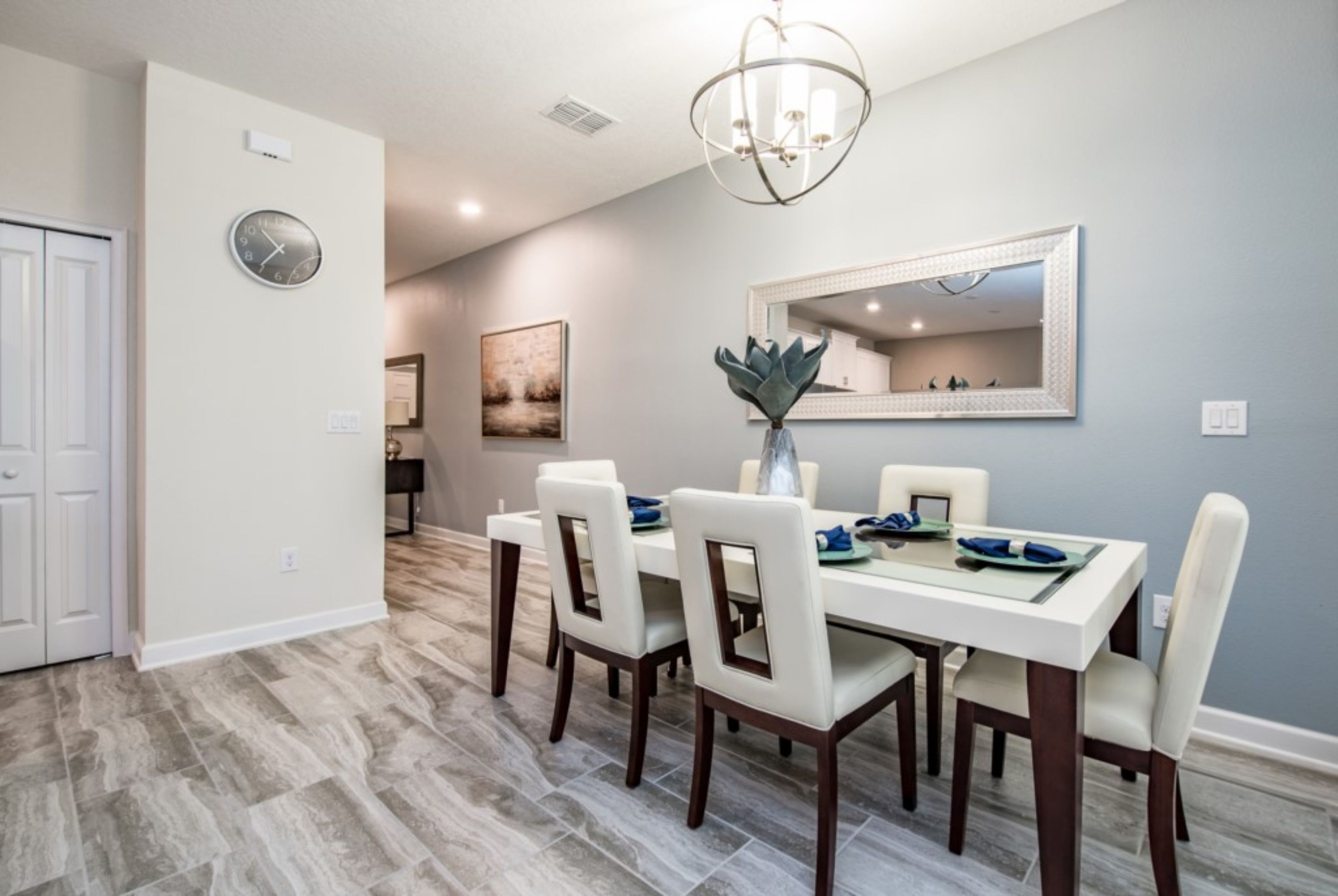 A dining area with a rectangular table, six chairs, a chandelier, a clock, and a mirror on the wall.