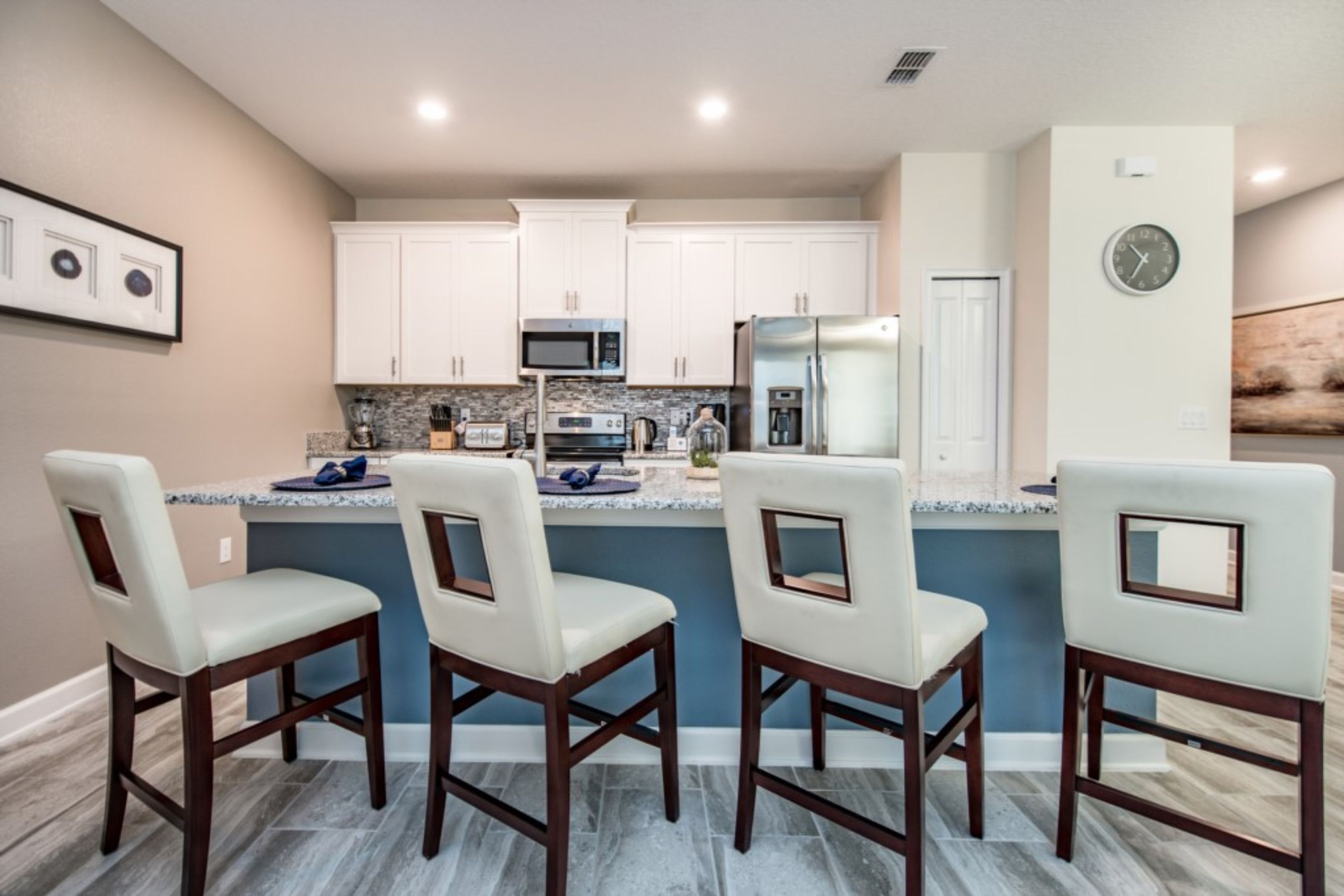 A modern kitchen with white cabinets, a central island with bar stools, and a clock on the wall.