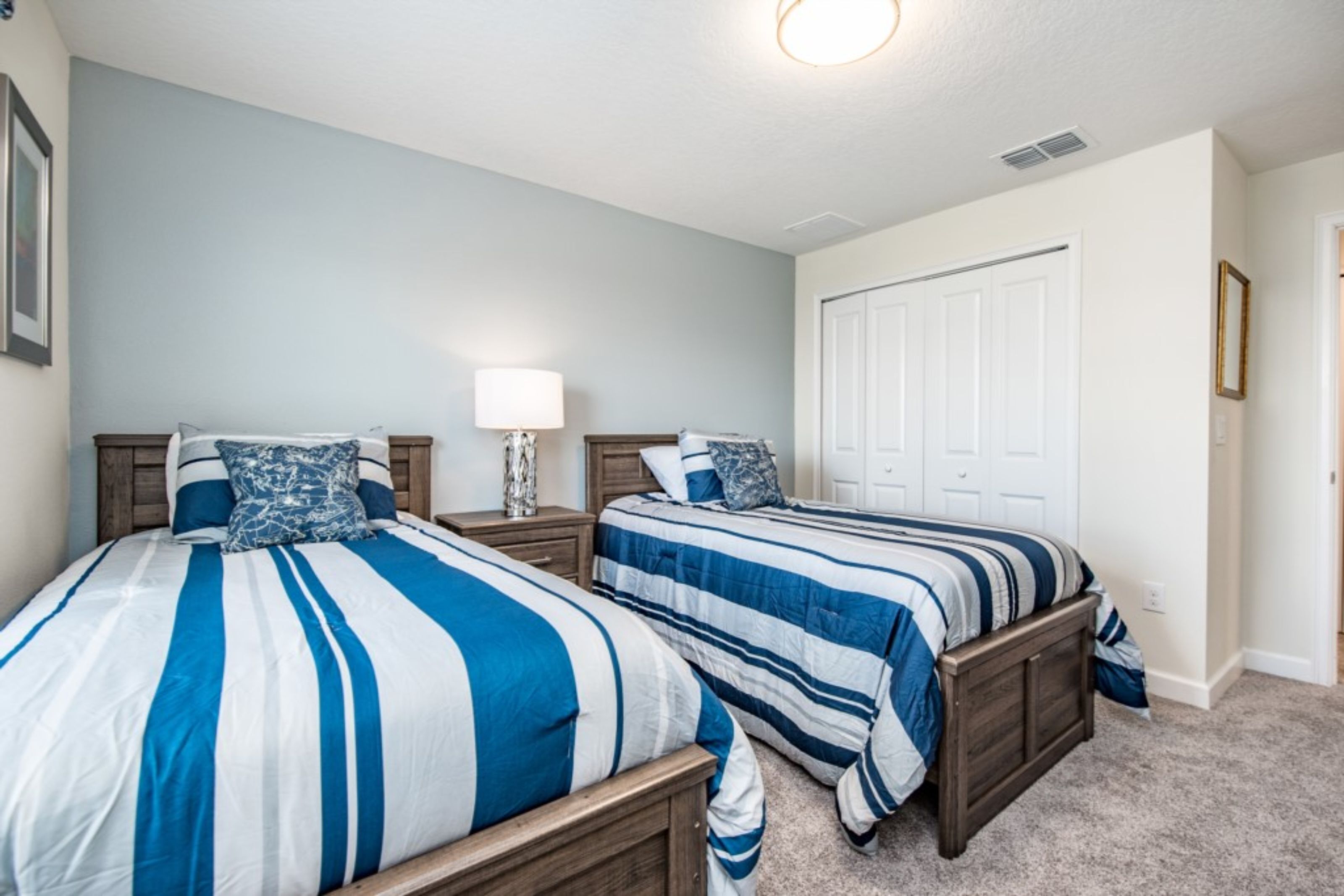 A bedroom with two beds, a nightstand, a lamp, and a door.