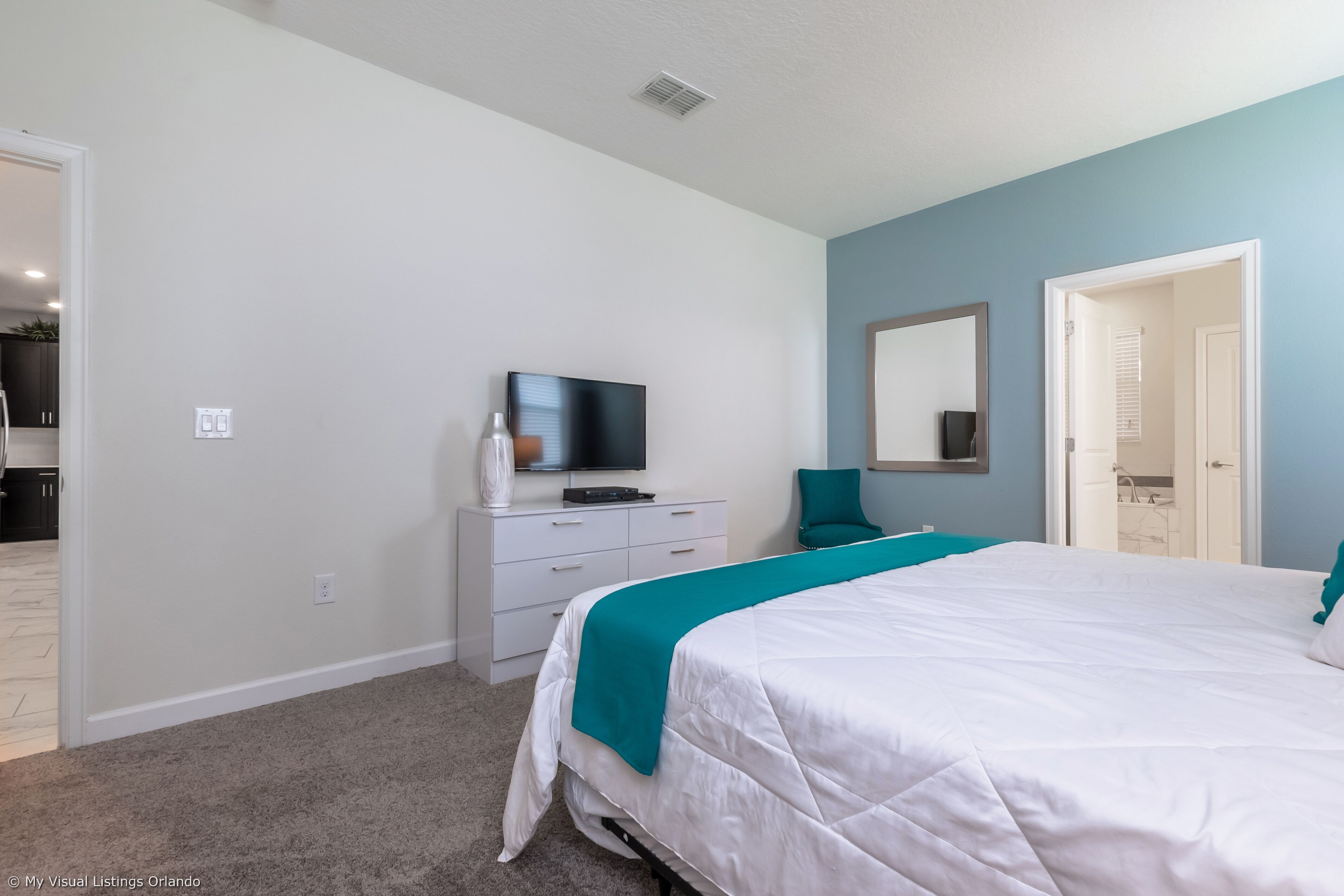Quarto com uma cama, uma TV sobre uma cômoda, um espelho e uma porta que dá para outro espaço.
