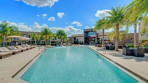 A pool area with lounge chairs, palm trees, and a modern building in the background.