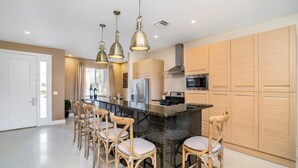 A modern kitchen with a central island, bar stools, stainless steel appliances, and wooden cabinets.