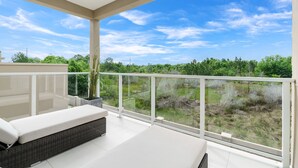 A balcony with a white sofa and a potted plant, overlooking a grassy area and trees.