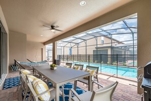 Un porche techado con vista a la piscina, mobiliario exterior y ventilador de techo.