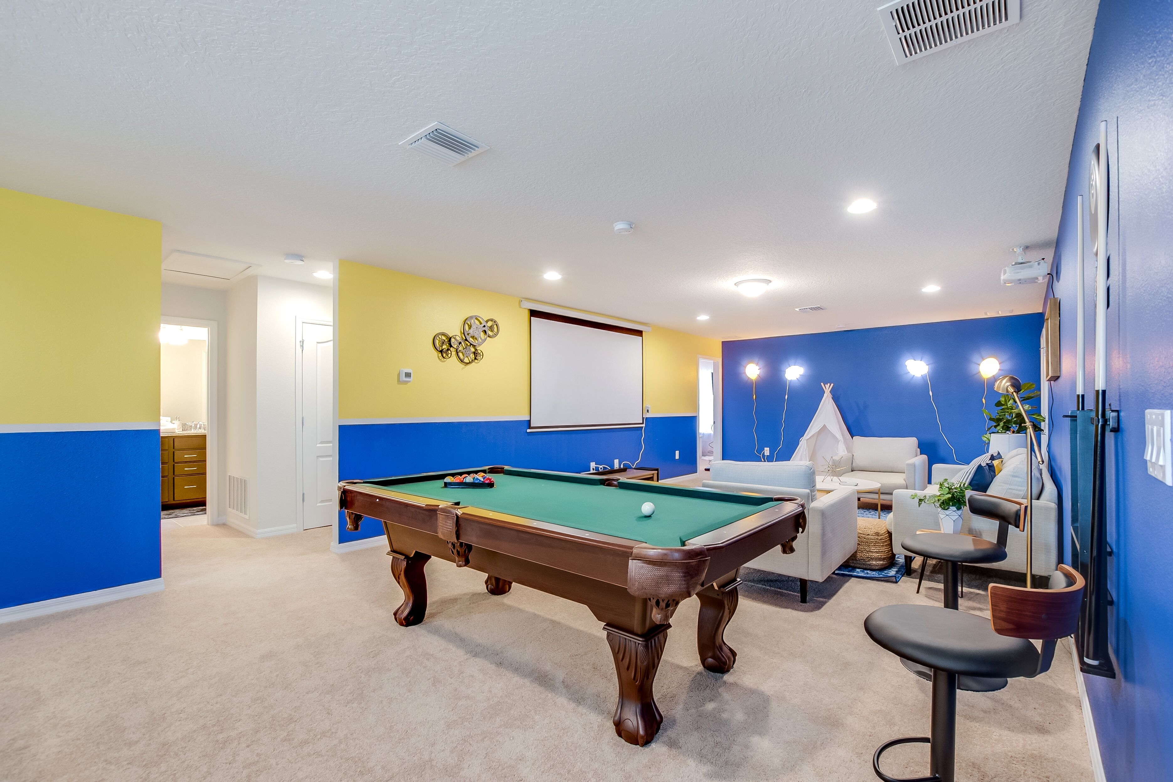 A pool table in a room with blue and yellow walls, a whiteboard, and a seating area with a lamp.