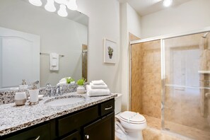 A modern bathroom with a granite countertop, white fixtures, a glass shower enclosure, and a framed picture on the wall. - 4582terra (Davenport)