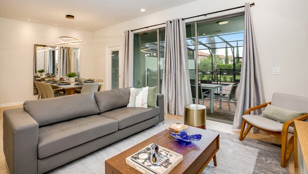 A modern living room with a grey sofa, a wooden coffee table, and a dining area with a glass door leading to an outdoor patio. - 4582terra (Davenport)