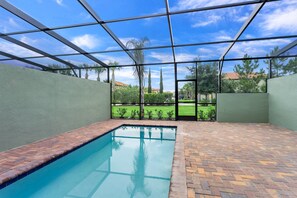A swimming pool with a brick border, surrounded by a glass enclosure with a view of a green landscape and buildings. - 4582terra (Davenport)