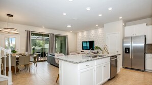 A modern kitchen with a large island, stainless steel appliances, and a dining area with a glass door to the outdoors. - 4582terra (Davenport)