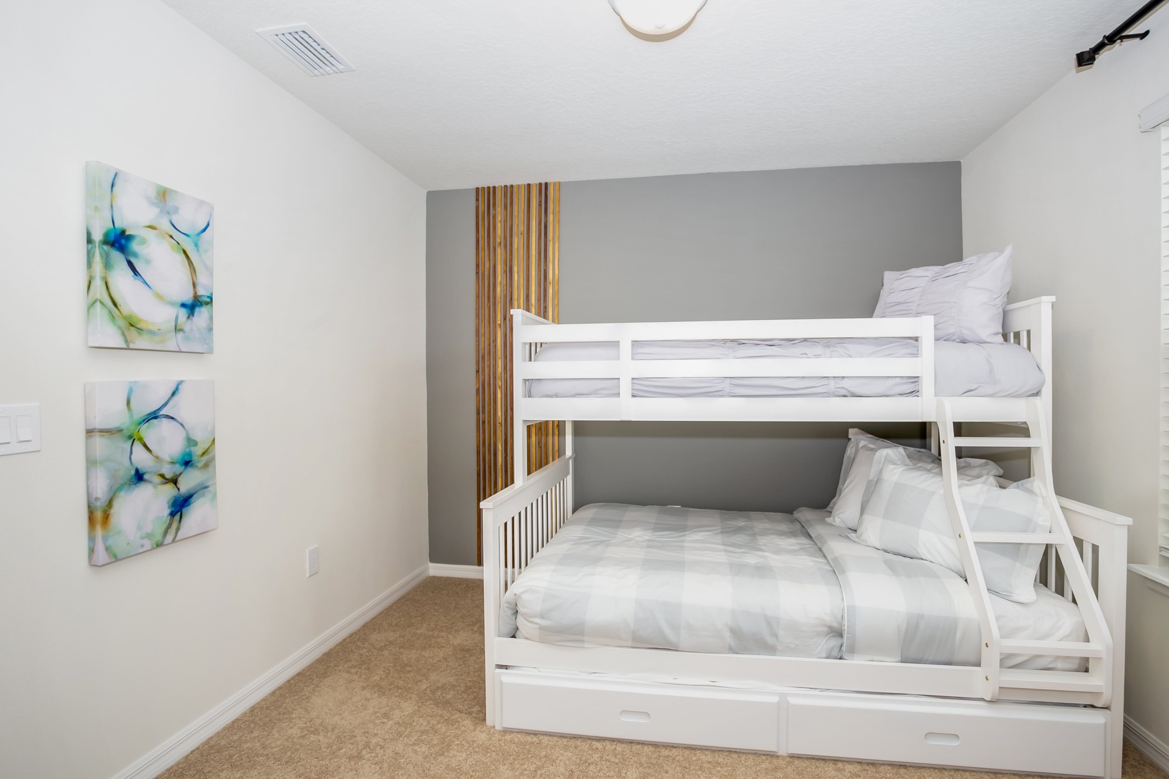 A bunk bed room with a grey wall, a wooden slat divider, and two abstract paintings.