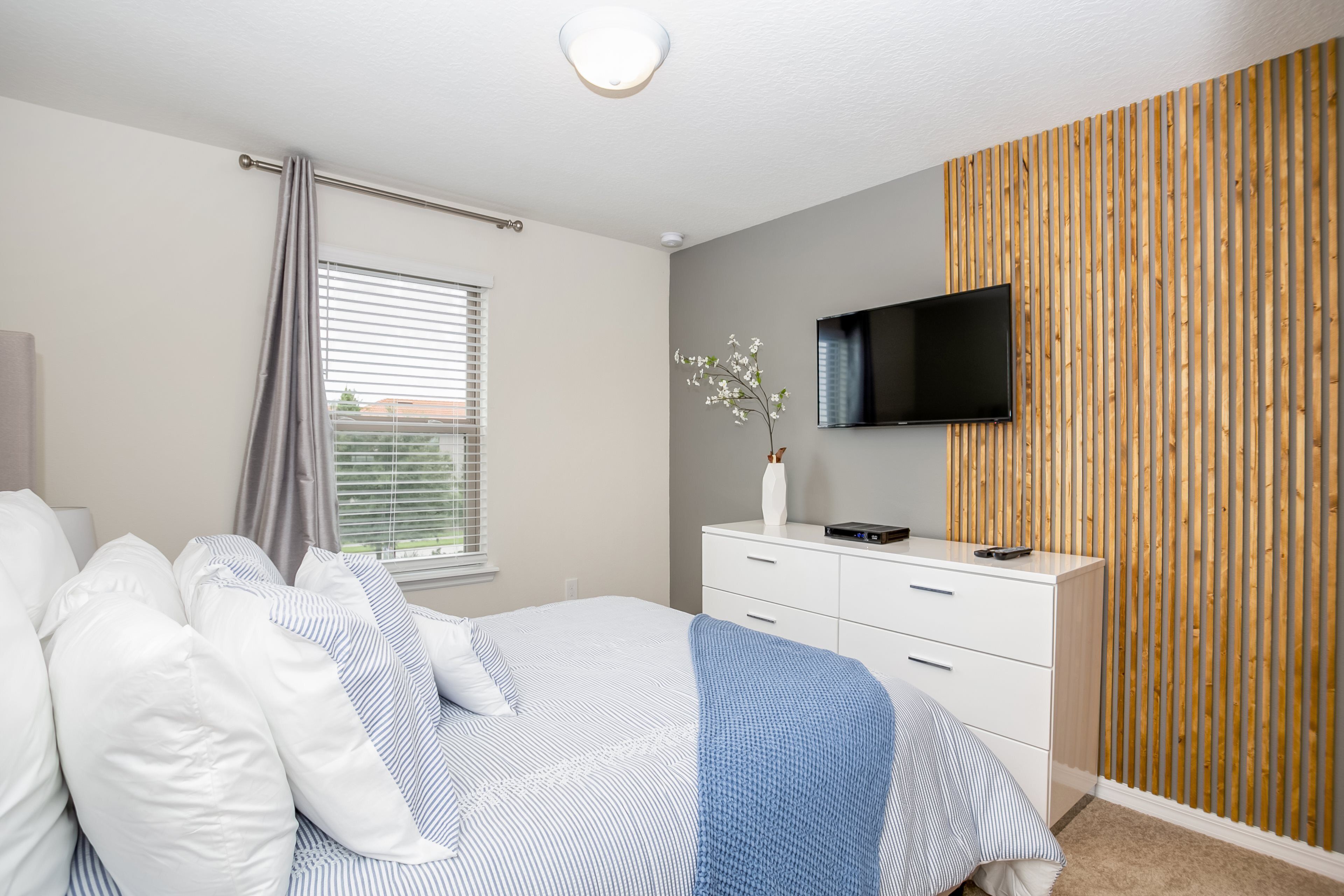 A bedroom with a bed, white dresser, TV, and wooden panel wall.