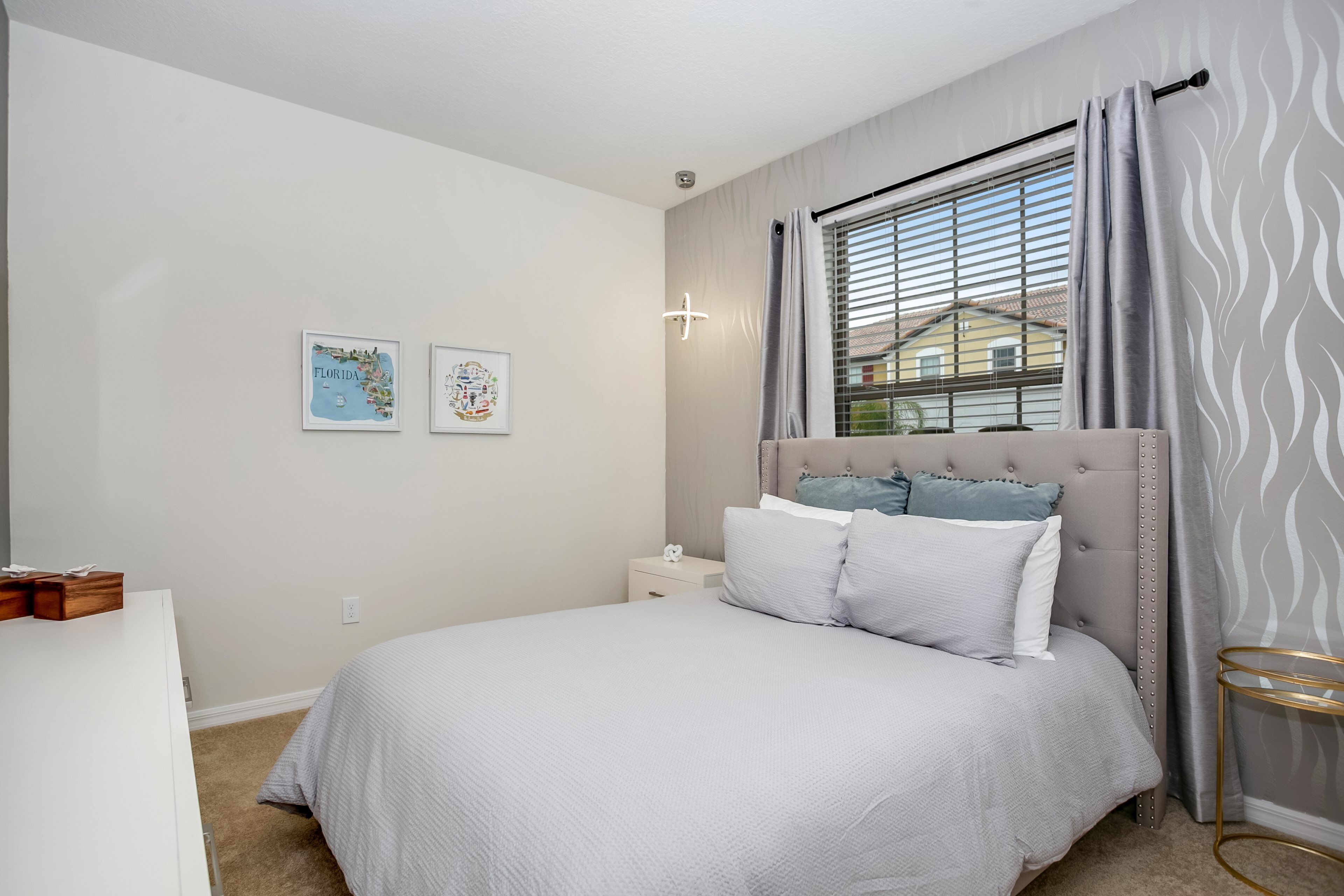 Een slaapkamer met een bed, nachtkastje, wandlamp en raam met gordijnen.