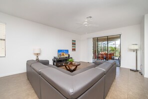 A spacious living room with a sectional sofa, a coffee table, a TV, and a sliding glass door to the outdoors.