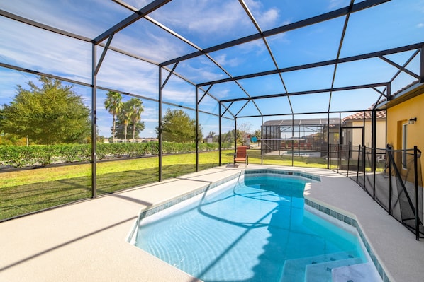 A swimming pool with a glass enclosure, surrounded by a patio area and a view of a residential neighborhood.