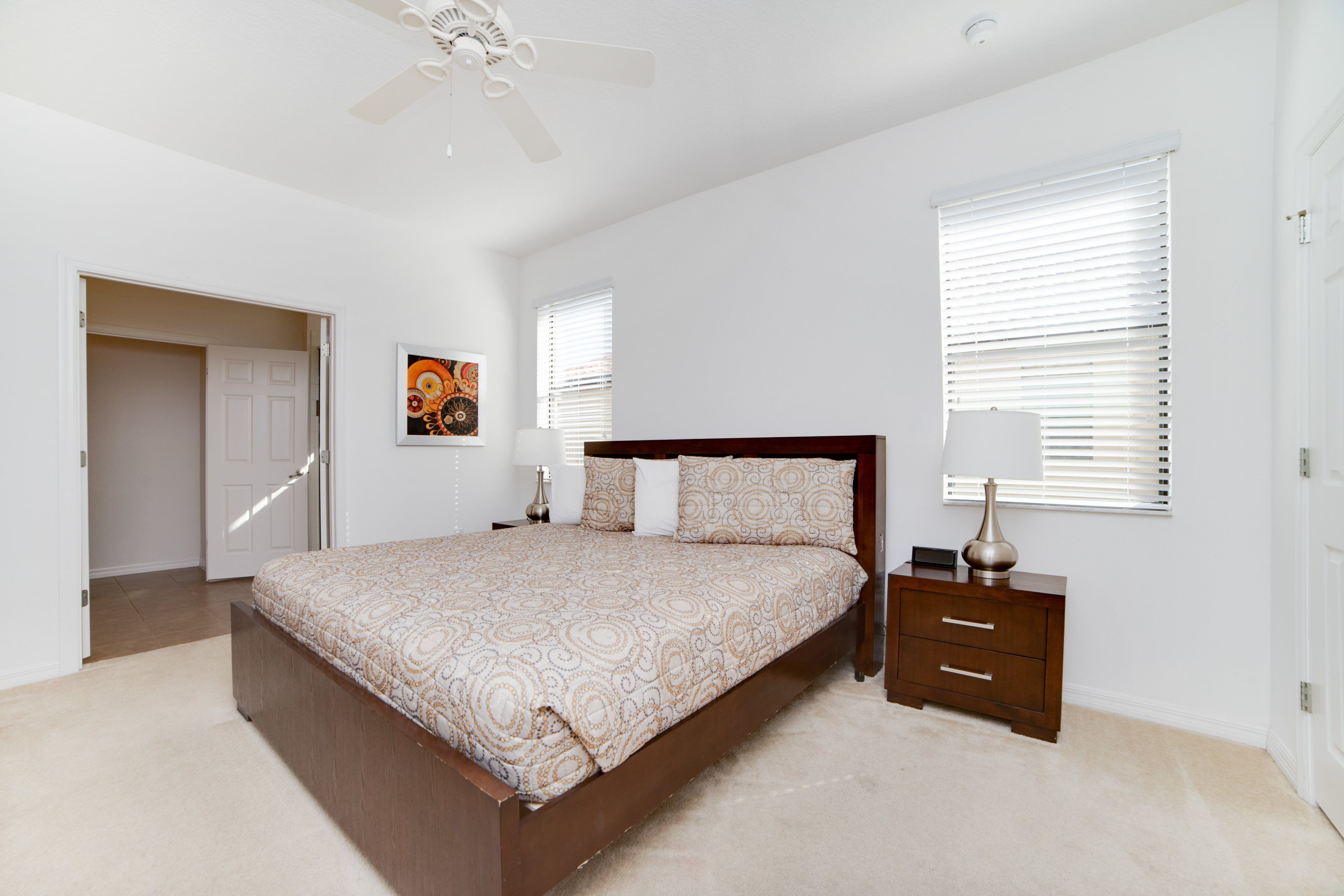 A bedroom with a bed, a nightstand, a lamp, a ceiling fan, and a door.