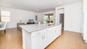A spacious kitchen with a central island, white cabinetry, and a large window providing natural light. - 2509rose (Davenport)
