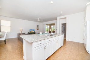 A spacious kitchen with a central island, white cabinetry, and a large window providing natural light.