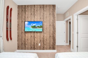 Quarto com parede de destaque em madeira, uma TV exibindo uma cena de praia e duas camas.