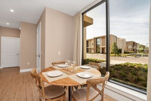 Uma sala de jantar com uma mesa redonda posta para quatro pessoas, grandes janelas e vista para edifícios modernos.