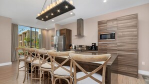A modern kitchen with a central island, wooden chairs, and a stainless steel refrigerator. - 4bdrm at Magice Village Resort (Kissimmee)