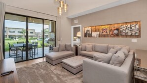 A modern living room with a sectional sofa, a dining table, and a large sliding glass door leading to an outdoor patio. - 4bdrm at Magice Village Resort (Kissimmee)