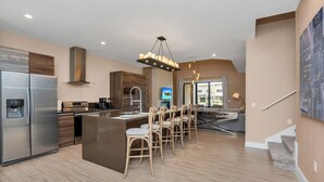 A modern kitchen with a central island, stainless steel appliances, and wooden chairs. - 4bdrm at Magice Village Resort (Kissimmee)