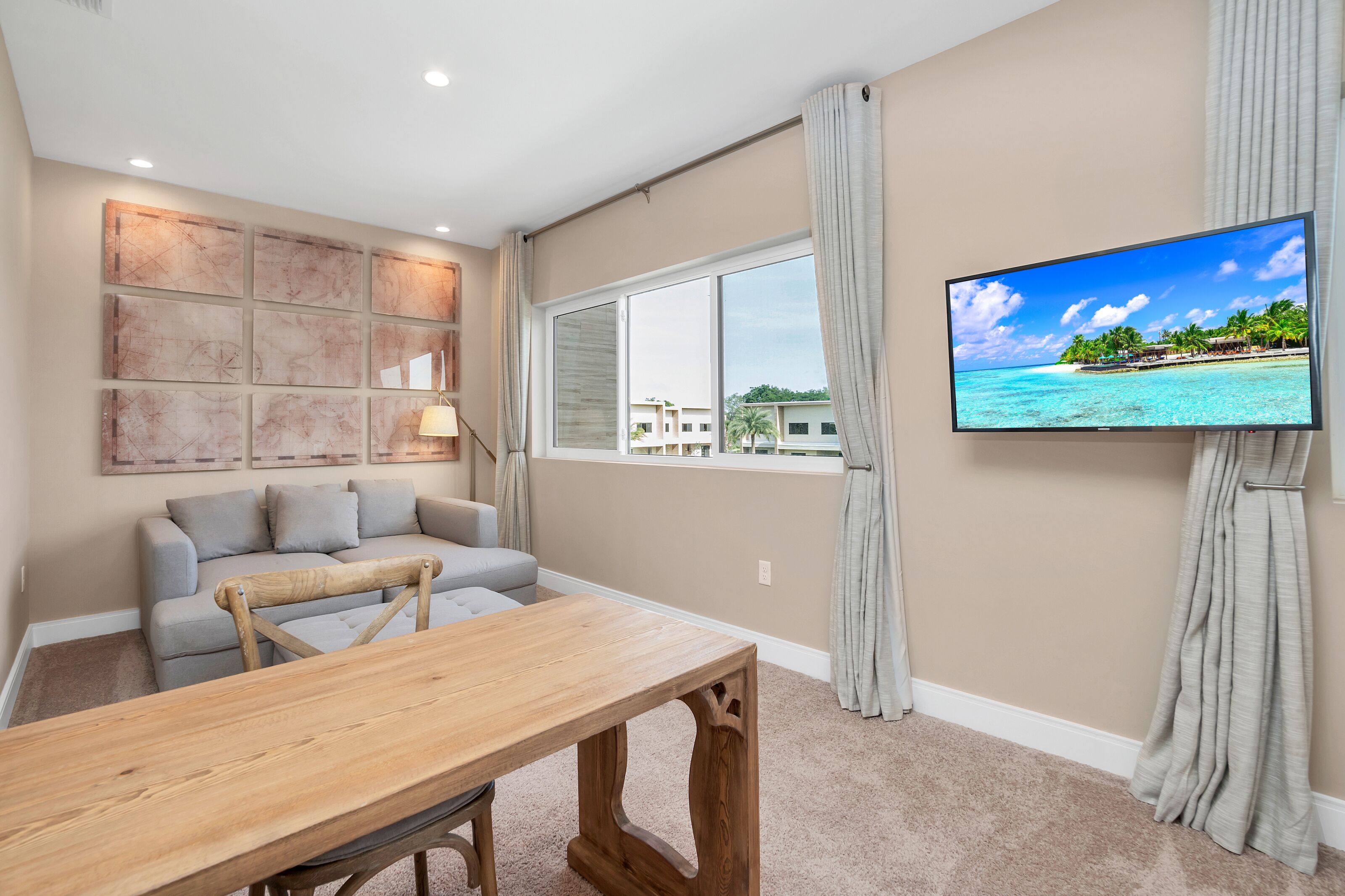 A living room with a wooden table, grey sofa, and a TV displaying a beach scene.