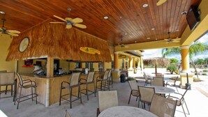 Zona bar all'aperto con tetto in paglia, soffitto in legno e diversi posti a sedere.