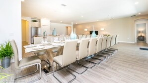 Un espace repas moderne avec une longue table, plusieurs chaises et une cuisine en arrière-plan.