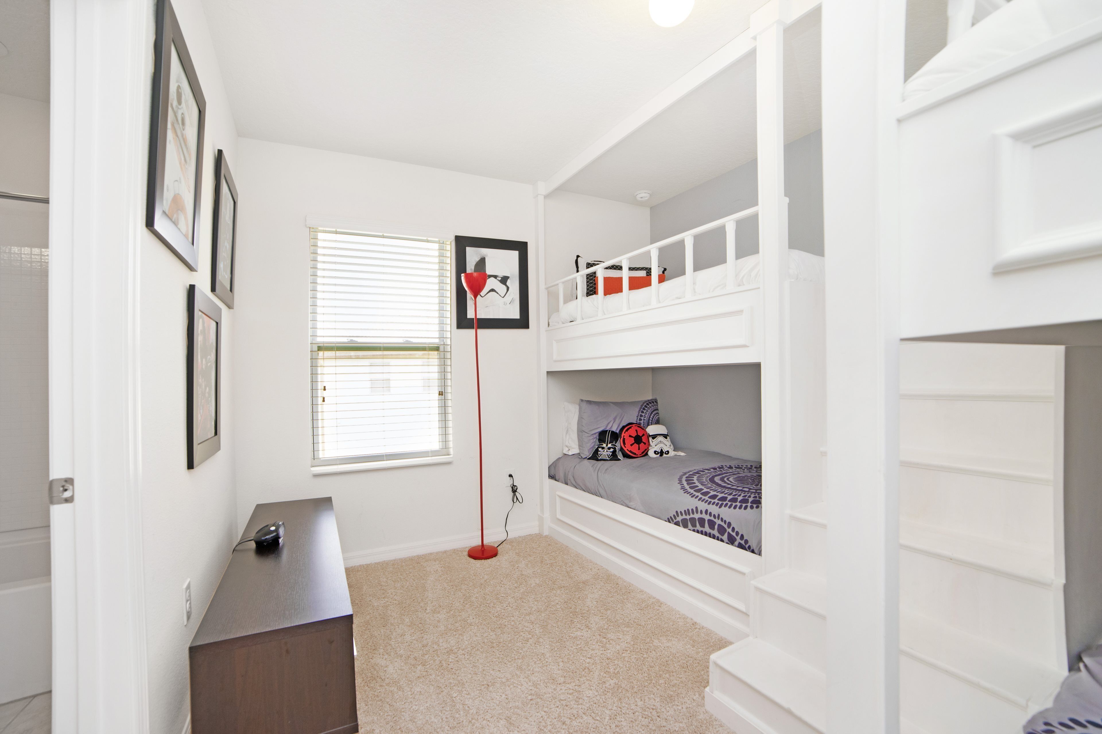 A bedroom with bunk beds, a desk, and a window with blinds.