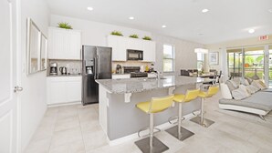 Eine moderne Küche mit weißen Schränken, einem Edelstahlkühlschrank und einer Kücheninsel mit Marmorplatte und Barhocker.